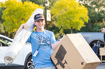 college student carrying a box and rug to a dorm room
