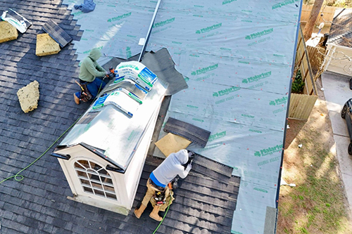 person outside crawling on top of a building adding roofing - Photo Credit Noble Roofing